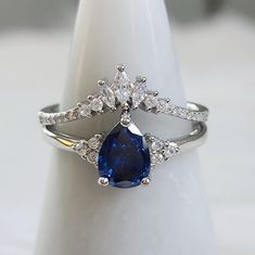 a blue and white diamond ring sitting on top of a white cloth covered tablecloth