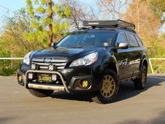 a black subarunt is parked in a parking lot with trees and bushes behind it