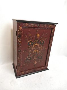 a red and gold painted cabinet with floral designs on the front, sitting against a white wall