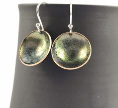 "A beautiful delicate pair of bronze green \"bowl\" shaped earrings hanging on sterling silver 925 hook wires, perfect for everyday wear. Copper discs were domed into little \"bowls\" and filled with bronze enamel and fired at 900 degrees. Several layers of enamel were applied to create patterns, depth and colour. The back of the earrings have been enamelled in black to provide strength and comfort. A perfect way to add a pop of colour to your jewellery collection or a gift for someone special. Green Round Pendant Earrings For Gift, Round Black Enamel Earrings As Gift, Nickel-free Enamel Round Earrings, Circular Earrings, Bronze Green, Iridescent Green, Disc Earrings, Disc Necklace, Enamel Earrings