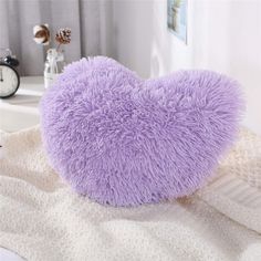 a purple heart shaped pillow sitting on top of a bed next to a white blanket