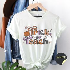 Show your students your love for Halloween and teaching with this cute Trick or Teach tee! Perfect to wear on Halloween or during the fall season, or give as a spooky gift to a teacher friend or coworker. Find more spooky season tops and sweatshirts here: https://www.etsy.com/shop/ConsiderItBliss?ref=search_shop_redirect&section_id=35296852 These super soft Bella Canvas tees are unisex sizing. Please double check the measurements provided in the listing before selecting a size. If you are not ce White T-shirt For School In Fall, Trendy School T-shirt For Fall, Trendy Fall T-shirt For School, Teacher Shirts For Halloween, Halloween Tshirt Ideas For Teachers, October Teacher Shirts, Trick Or Teach Shirt, Teach Shirt, Spooky Orange Fall T-shirt