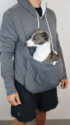 a man in grey hoodie holding a white and gray dog inside his back pocket