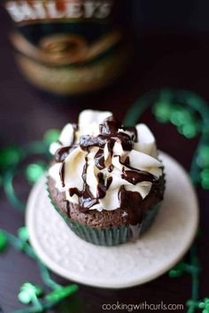 a chocolate cupcake topped with whipped cream and chocolate shavings on a white plate