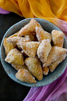 powdered sugar coated pastries in a blue bowl on a purple and yellow cloth