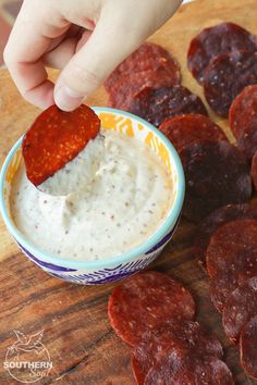 a person dipping some kind of sauce in a bowl on top of food patties