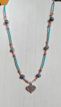 "This necklace is made with turquoise seed beads, pink seed beads, blue crackled beads, tan seed beads, and a heart \"daughter\" pendant in the middle. Toggle clasp. Measures 19 inches long end to end." Blue Dangle Beaded Necklace With Tiny Beads, Adjustable Turquoise Necklaces With Tiny Beads, Adjustable Single Strand Turquoise Beaded Necklace, Adjustable Turquoise Single Strand Beaded Necklace, Adjustable Beaded Turquoise Necklace, Adjustable Blue Beaded Turquoise Necklace, Adjustable Turquoise Heishi Bead Necklaces, Adjustable Turquoise Beaded Chain Necklace, Adjustable Turquoise Beaded Necklace With Tiny Beads