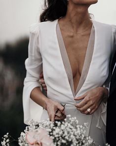 a man and woman standing next to each other in front of a white wall with flowers