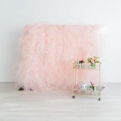 a shelf with flowers and tea cups on it in front of a fluffy pink backdrop