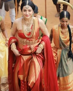 a woman in a red and gold sari sitting on the ground with other people around her