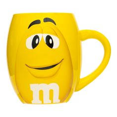 a yellow coffee mug with m on it's side and eyes drawn in the shape of a smiley face