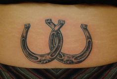 a woman's lower back tattoo with two horseshoes in the shape of letters u