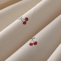 white fabric with cherries embroidered on the back and side of each piece in red