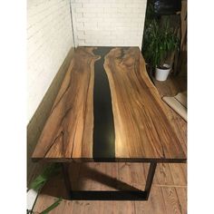 a table made out of wood and metal with black stripes on the edge, sitting in front of a brick wall