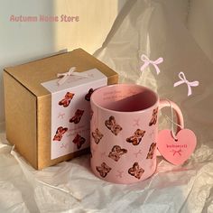 a pink coffee mug sitting on top of a white table next to a cardboard box