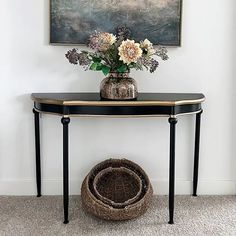 a vase with flowers sitting on top of a table next to a basket and painting