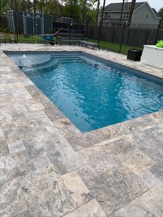 an empty swimming pool in the middle of a backyard area with concrete pavers and black fence