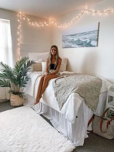 a woman sitting on top of a bed next to a potted plant and rug