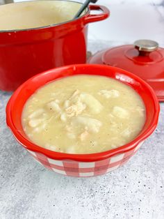 a red bowl filled with soup sitting on top of a counter next to a pot