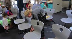 a group of children and adults playing with chairs in a room filled with toys, books, and other items