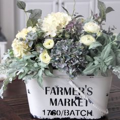 a white bucket with flowers and greenery in it