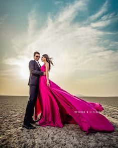 a man and woman in formal wear standing on the beach with their arms around each other