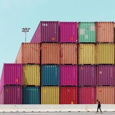 a man walking past a large stack of colorful shipping containers