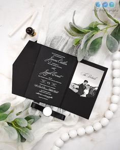 the wedding stationery is laid out on a table with greenery and beads around it