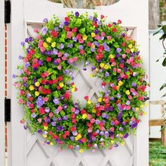 a colorful wreath is hanging on the side of a white gate with flowers all over it