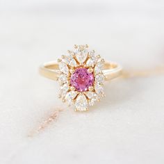 a close up of a ring with a pink stone in the center and white diamonds around it