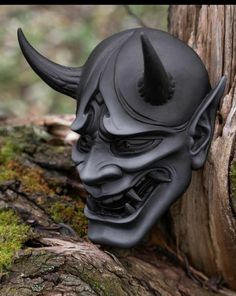 a black mask with horns on it sitting next to a tree