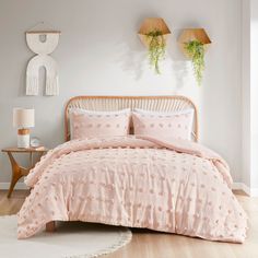 a bed with pink comforter and pillows in a room next to two plants on the wall