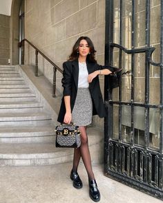 a woman standing in front of a door holding a purse and posing for the camera