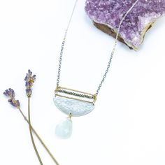 Embrace the enchanting allure of our Moonstone Radiance Necklace, a harmonious blend of celestial elegance and artistic craftsmanship. At its heart, a large moonstone, glowing with an ethereal light, gracefully hangs from a textured silver half circle, capturing the essence of lunar mystique. Above, a delicate gold rectangle, meticulously adorned with tiny sparkling pyrite gemstones, stretches the length of the disc, adding a touch of subtle brilliance to the design. The interplay of textures an Artisan Silver Necklace With Moon Phase Detail, Artisan Silver Necklace With Moon Phase, Artisan Silver Necklace With Moon Charm, Elegant Handmade Half Moon Jewelry, Artisan Silver Jewelry With Moon Phase, Elegant Crescent Moonstone Necklace, Elegant Handmade Half Moon Necklace, Artisan Moon Charm Necklaces, White Half Moon Celestial Jewelry