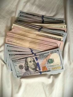 a pile of twenty dollar bills sitting on top of a white bed spread with sheets