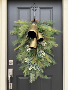 a christmas wreath with two bells hanging from the front door and evergreen branches around it