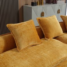 an orange couch with three pillows on it in front of a dresser and bookshelf