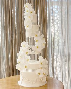 a three tiered wedding cake with white flowers on top and monogrammed initials