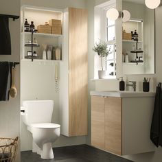 a white toilet sitting in a bathroom next to a wooden cabinet and sink under a window