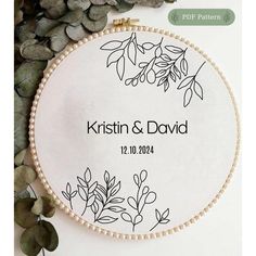 a white embroidered wedding ornament with leaves and berries on it, surrounded by greenery