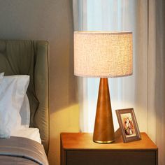 a lamp on a nightstand next to a bed with a framed photo and an empty picture frame