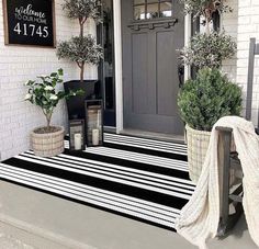 a black and white striped rug is on the front steps of a house with potted plants