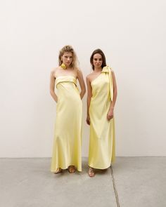 two women wearing yellow dresses standing next to each other in front of a white wall