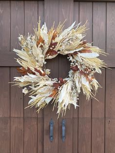 a dried wreath hanging on the side of a wooden door with two blue handles in front of it