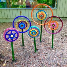 four colorful metal garden ornaments sitting on top of a patch of dirt in front of a building