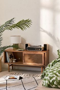 a room with a bed, plant and an old radio on the stand next to it