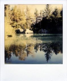 an image of a lake with trees in the background and some rocks on the shore