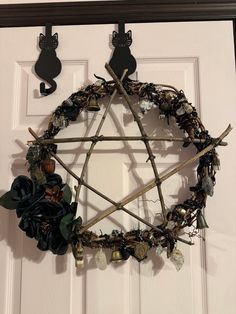 a wreath made out of branches and other items hanging on a door frame with two cats