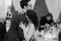 a man and woman hugging each other in front of a table with wine glasses on it