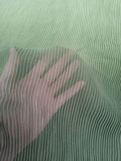 a person's hand is reflected in the glass on top of a bed sheet